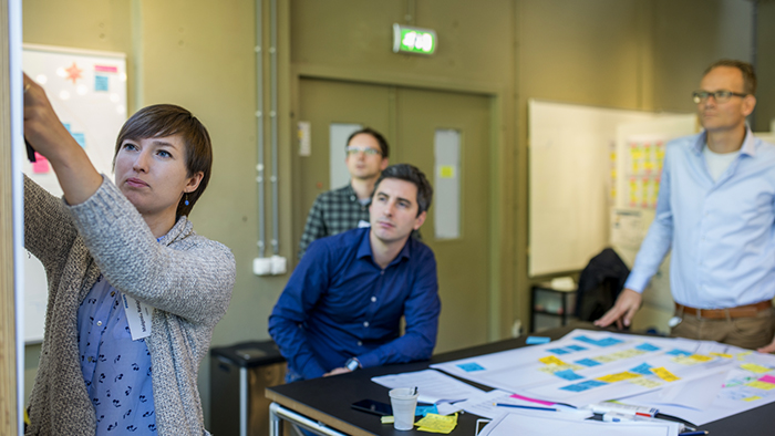 A woman in a conference room adds something to a whiteboard while coworkers look on