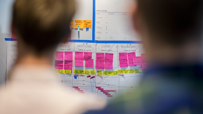 Two participants in a workshop look at a wall covered in sticky notes