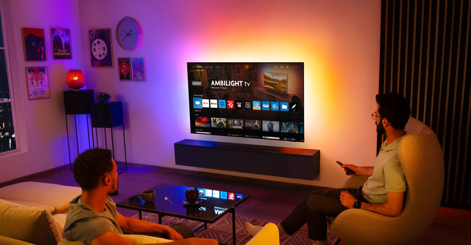 Двоє чоловіків дивляться телевізор Ambilight, закріплений на стіні у вітальні