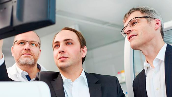 Three men &mdash; including two co-founders of Noscendo, Dr.  Philip Stevens and Dr. Peter Haug &mdash; look at a computer screen together. 